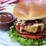 cooked cheeseburger on plate with a side bowl of bbq sauce
