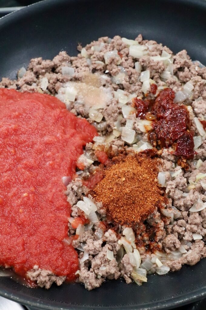 seasoned ground beef with a can of crushed tomatoes in a skillet