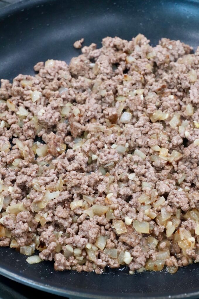 cooked ground beef with diced onions in a skillet
