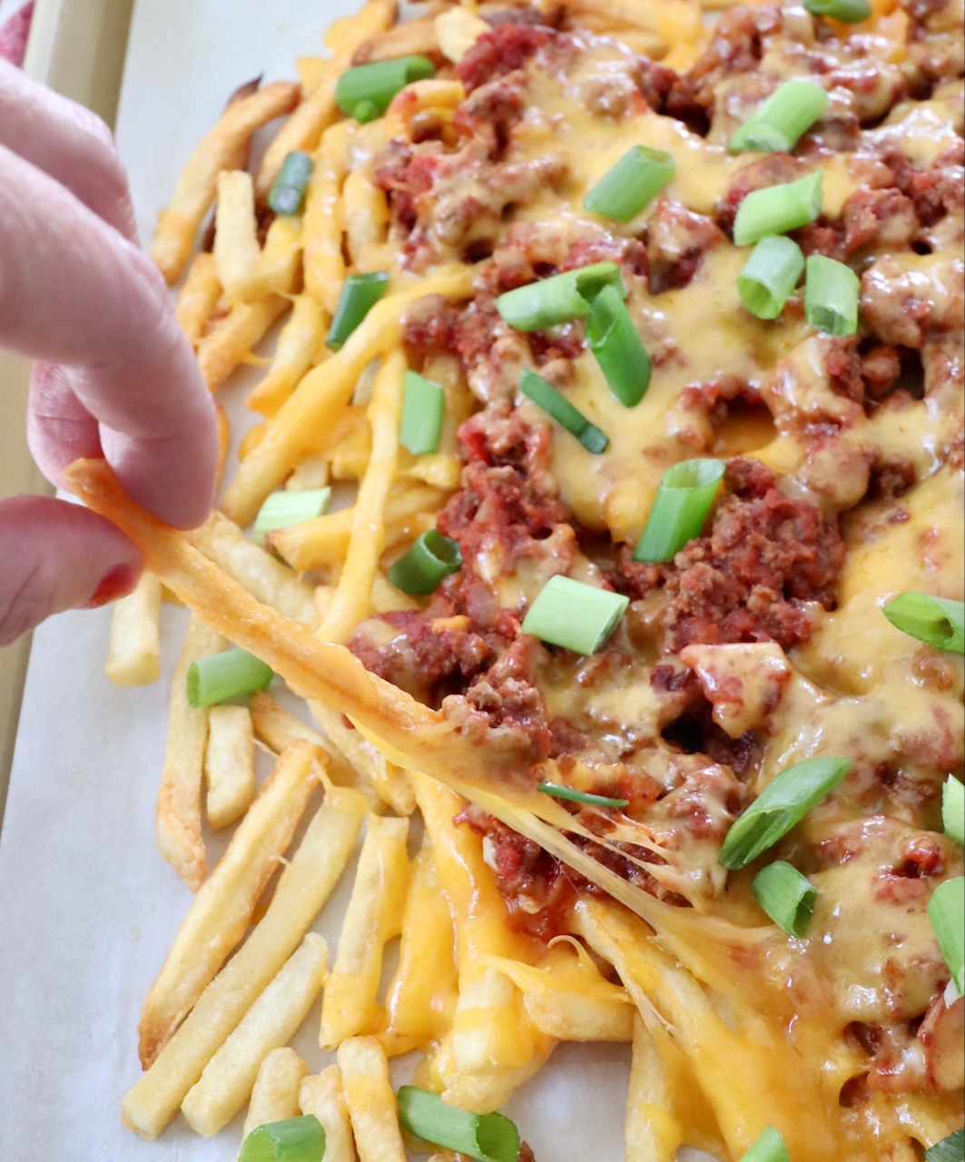 hand pulling cheese fry from baking sheet of chili cheese fries