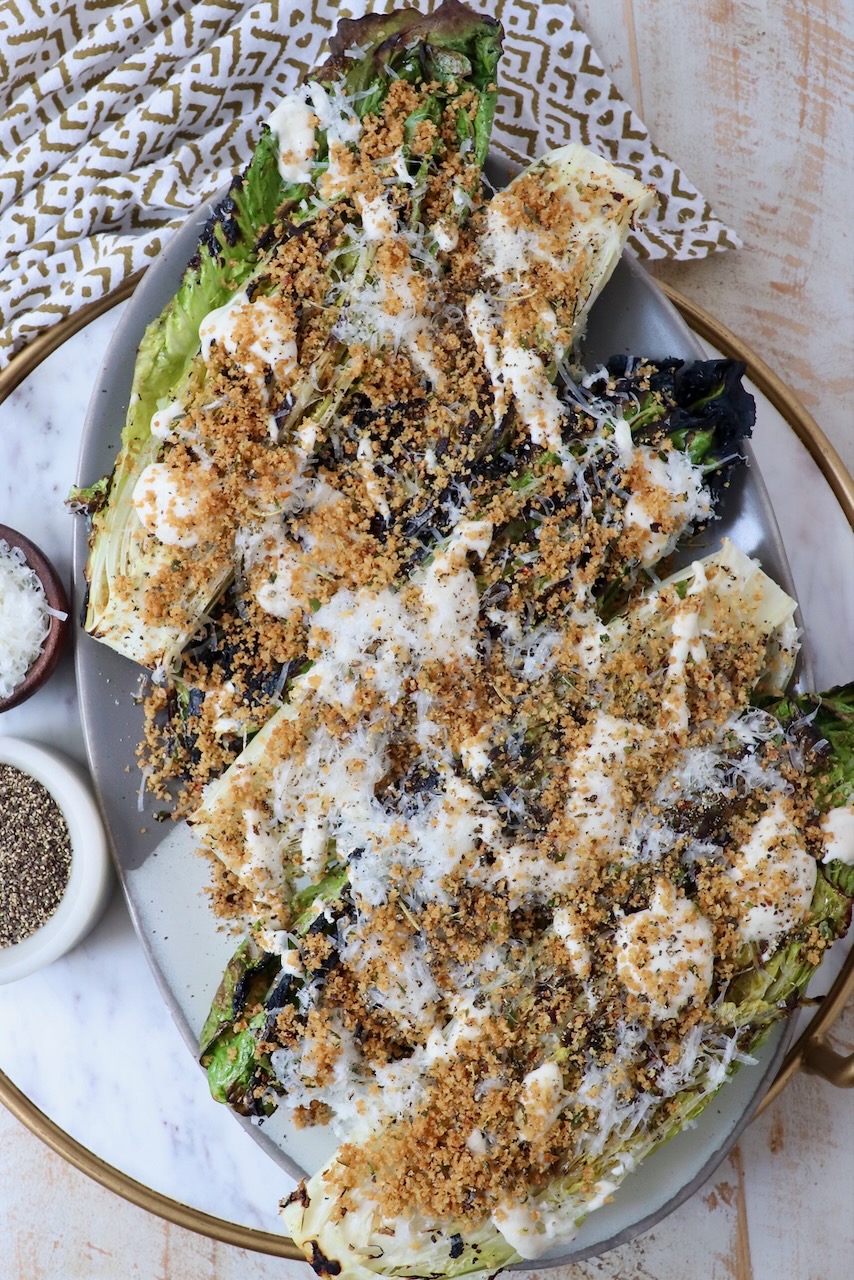 grilled caesar salad on serving platter topped with creamy dressing and toasted breadcrumbs
