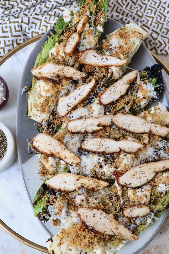grilled caesar salad on platter topped with sliced grilled chicken
