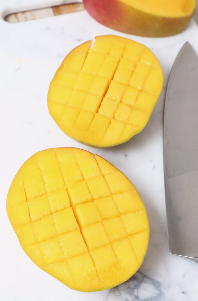 mango sliced into cubes on cutting board with knife
