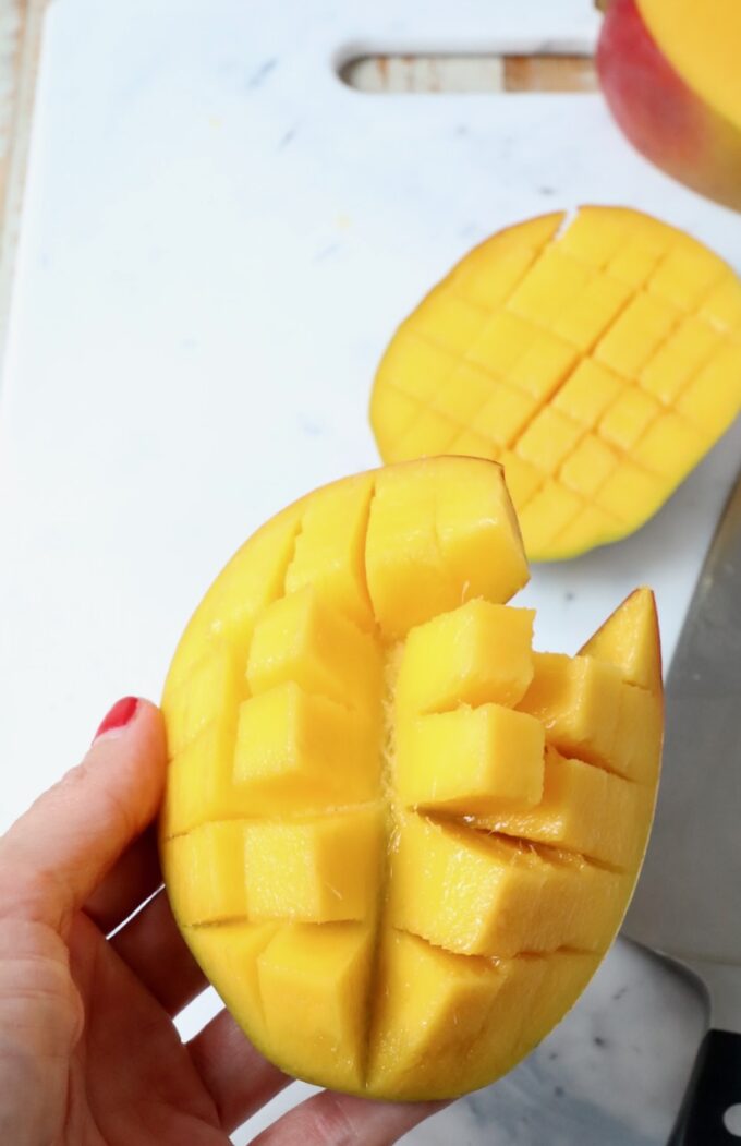 hand holding sliced mango over cutting board
