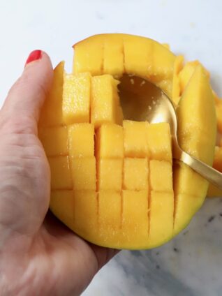 mango sliced into cubes in the skin with a spoon in the mango