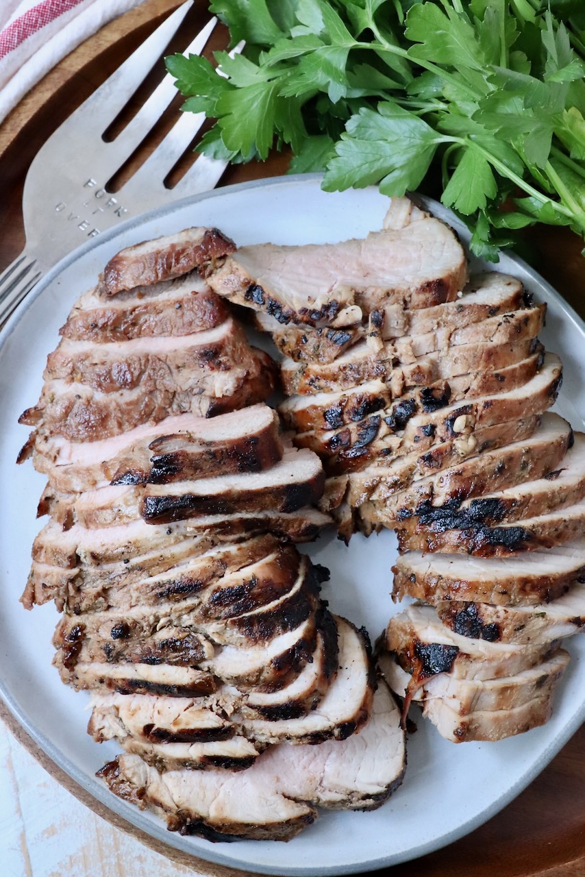 sliced pork tenderloin on plate with serving fork and fresh parsley on the side