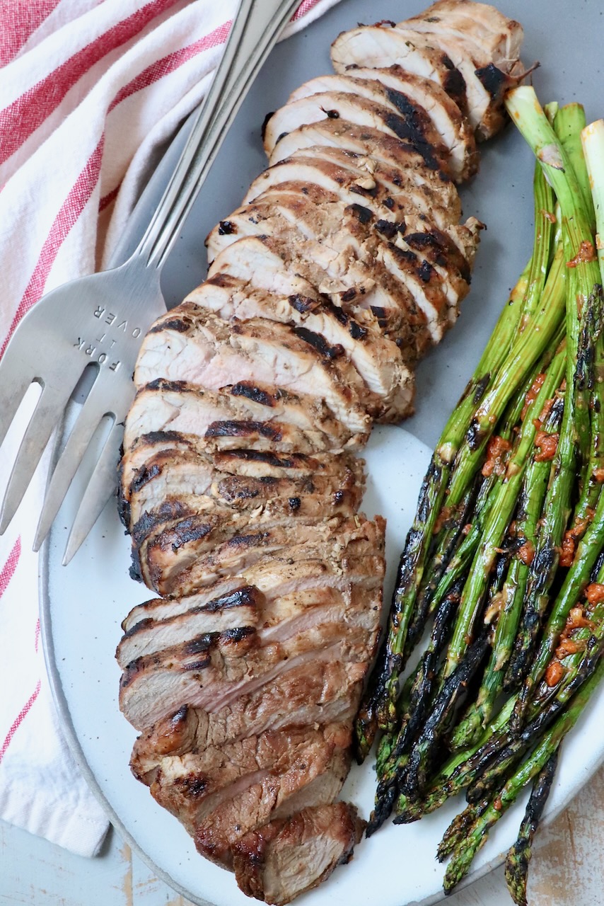 sliced grilled pork tenderloin on plate with grilled asparagus