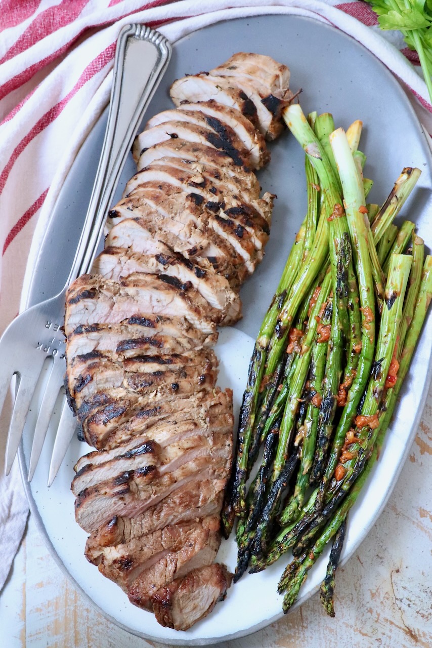 sliced pork tenderloin on plate with grilled asparagus