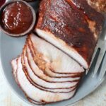 sliced smoked pork loin on plate with side bowl of bbq sauce