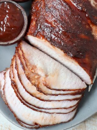 sliced smoked pork loin on plate with side bowl of bbq sauce