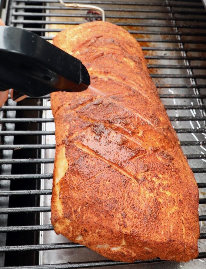 seasoned pork loin on smoker sprayed with apple juice