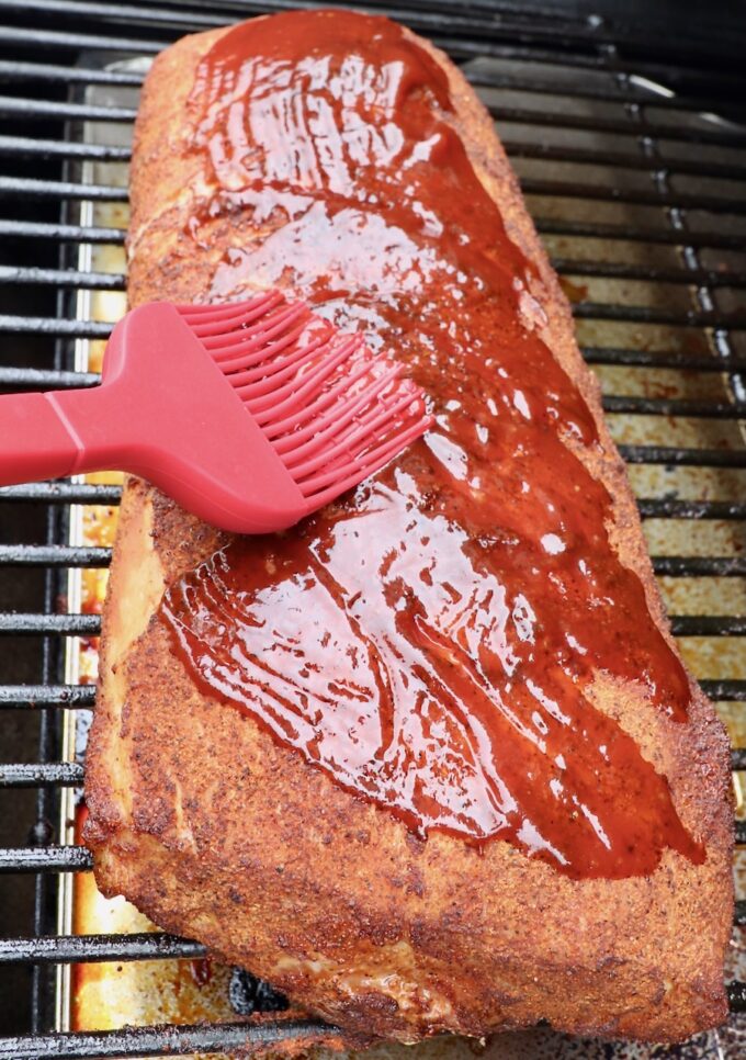 pork loin on smoker being brushed with bbq sauce