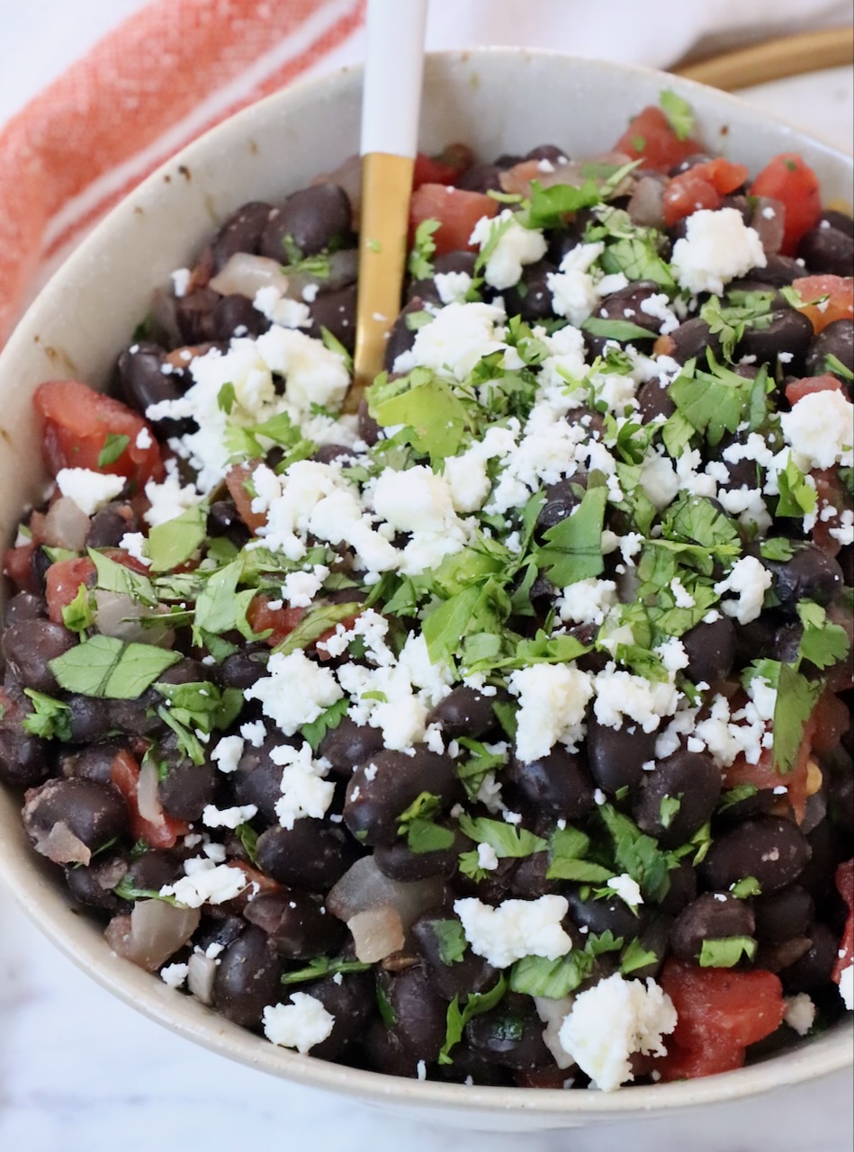 black beans in bowl topped with crumbled cheese and chopped cilantro