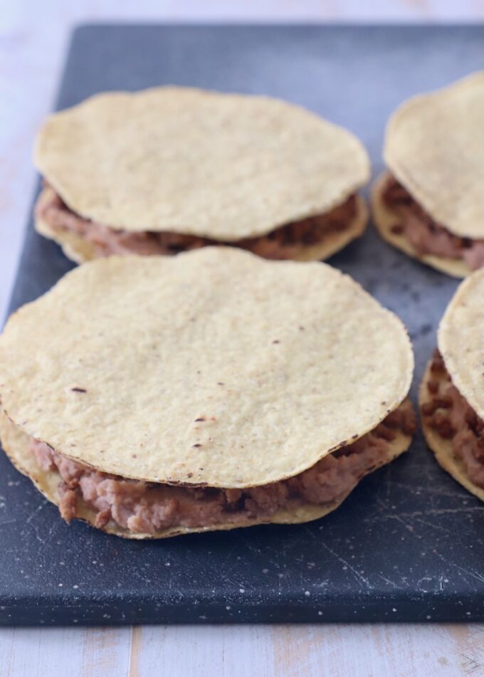 ground beef and refried beans sandwiched between tostada shells on a cutting board