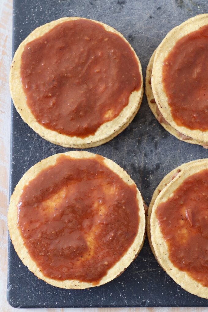 tostada shells topped with enchilada sauce on a cutting board