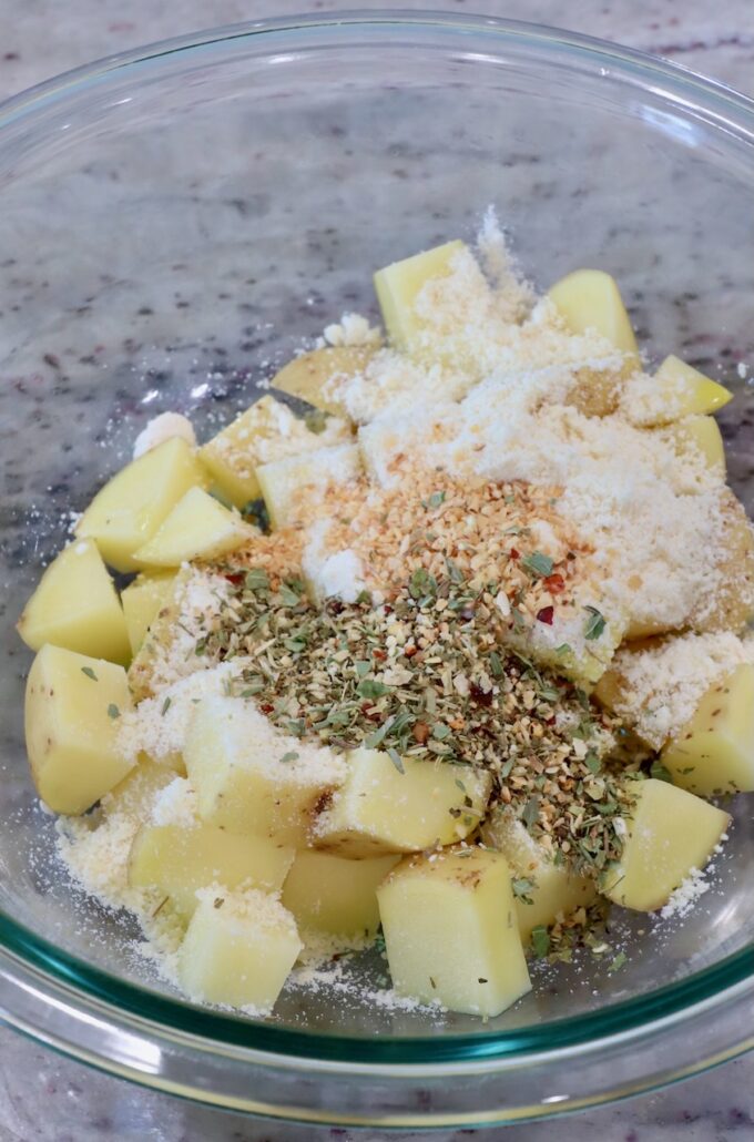 cubed potatoes with spices and parmesan cheese in glass bowl