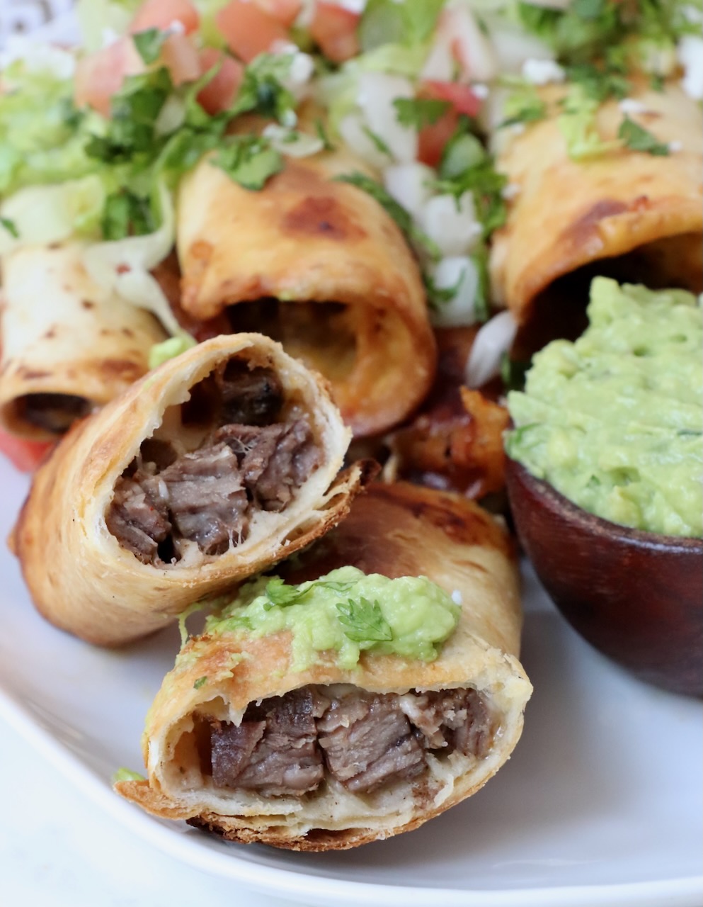 steak taquito cut in half on plate with guacamole