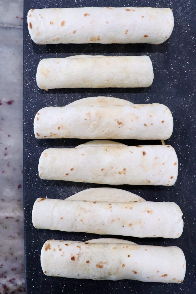 rolled up uncooked taquitos on cutting board