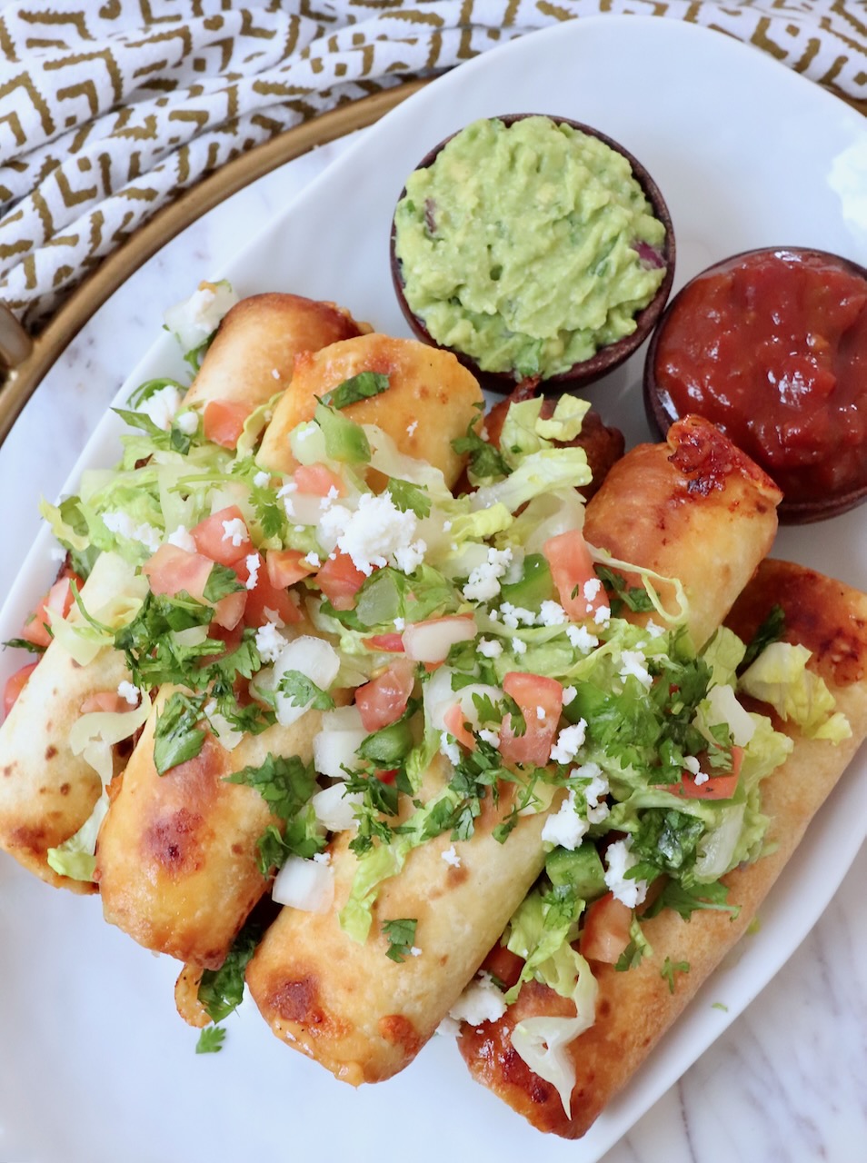 taquitos stacked up on plate topped with guacamole and pico de gallo