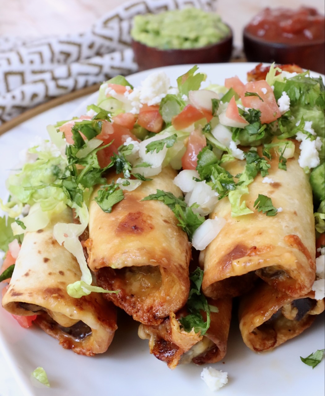 cooked beef taquitos stacked up on a plate topped with pico de gallo