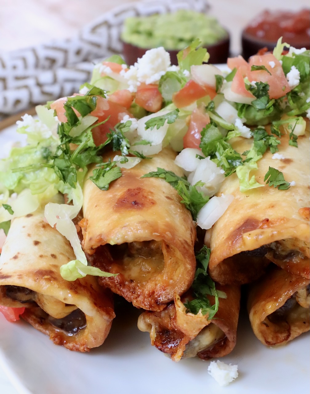 beef taquitos stacked up on plate topped with pico de gallo