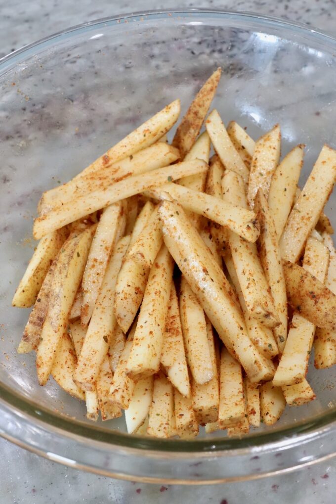 seasoned potatoes sliced into fries in glass bowl