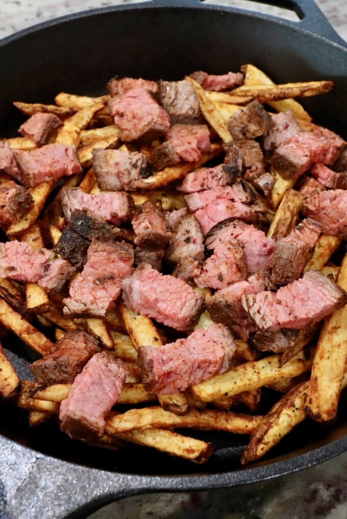 cooked french fries topped with diced grilled steak in cast iron skillet