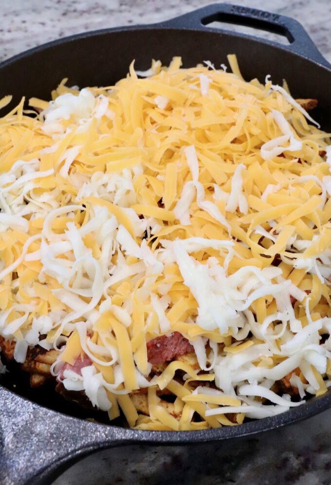 cooked french fries topped with diced grilled steak and shredded cheese in a cast iron skillet