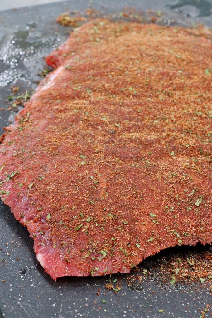 flank steak covered in seasoning on cutting board