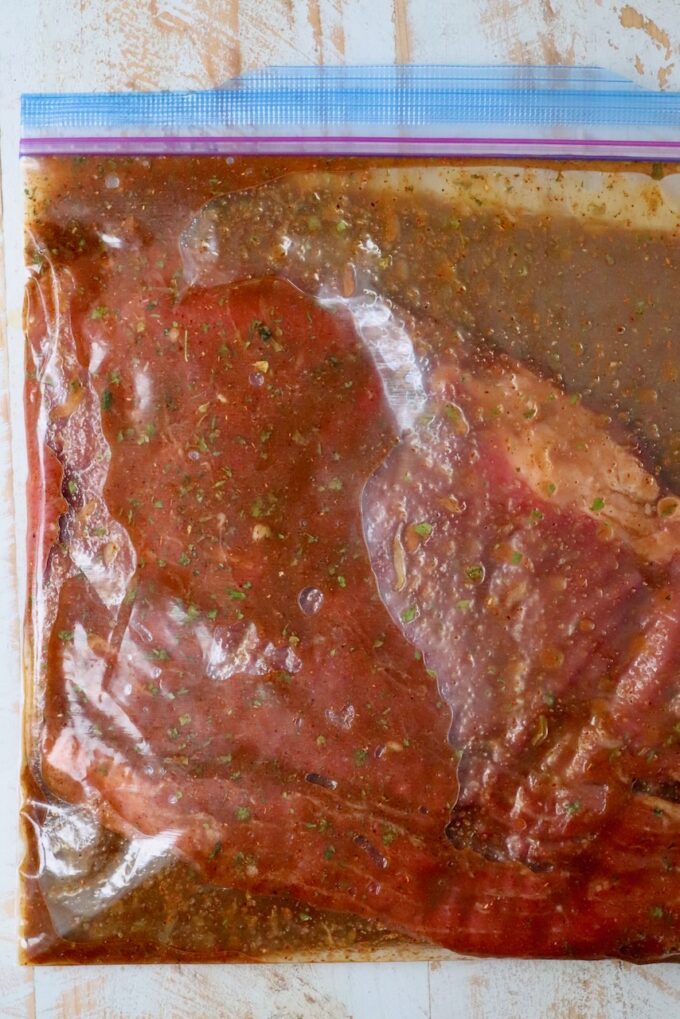 flank steak in bag of marinade on white wood board