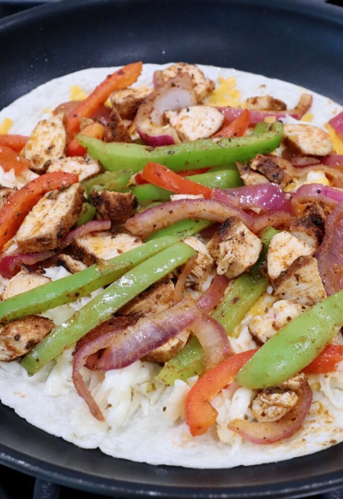 tortilla in a skillet topped with sliced fajita veggies and diced chicken