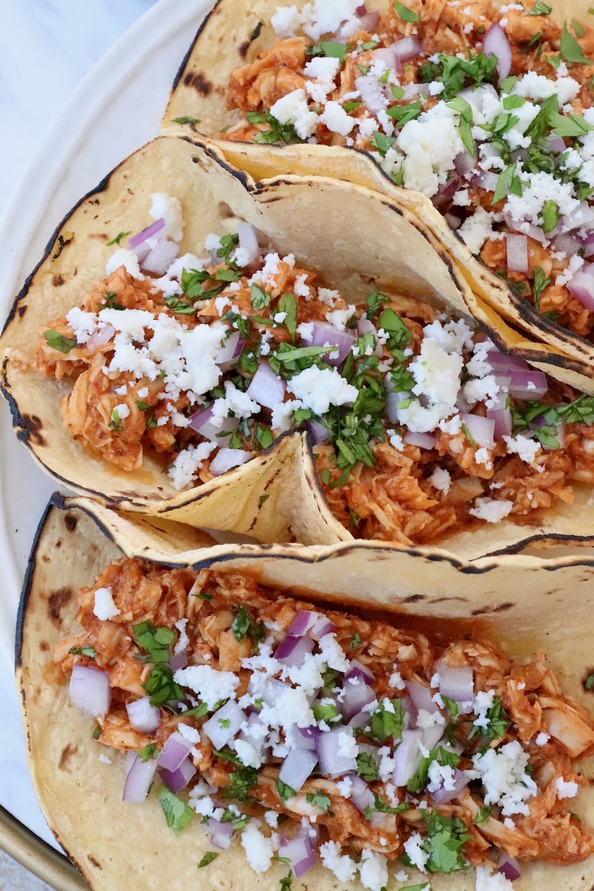 chicken tinga tacos on plate topped with diced onions and cilantro