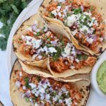 tacos on plate filled with cooked, shredded chicken, cheese, diced onions and cilantro