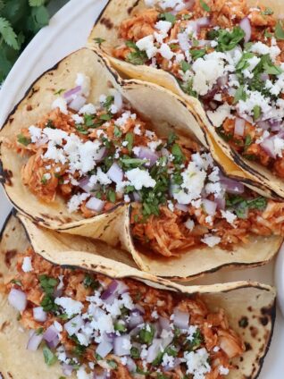 tacos on plate filled with cooked, shredded chicken, cheese, diced onions and cilantro