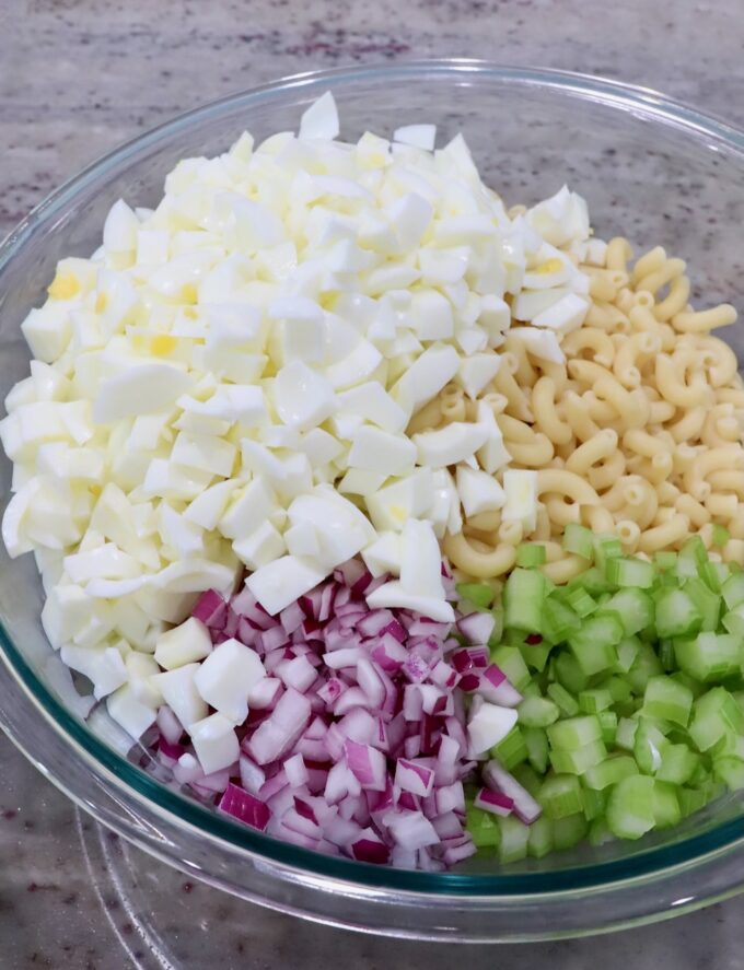 diced egg whites in a large glass bowl with cooked macaroni noodles, diced onions and diced celery