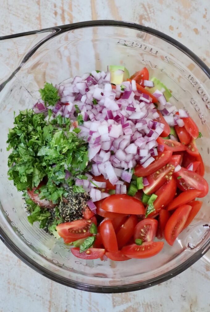 diced veggies in glass bowl with cilantro, salt and pepper
