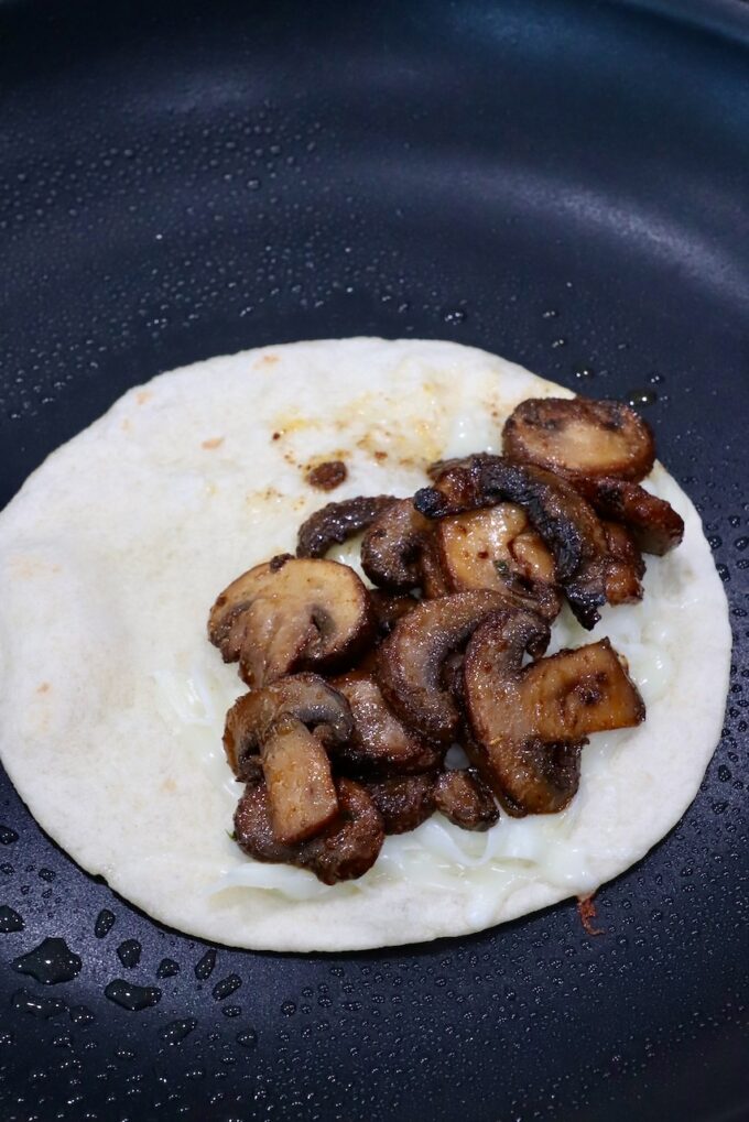 shredded cheese and sauteed mushrooms on tortilla in a skillet