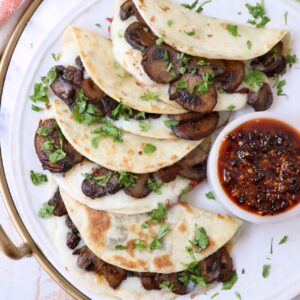 mushroom tacos stacked up on plate with a small bowl of salsa macha on the side