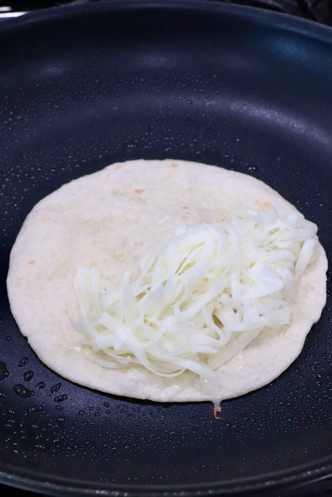 shredded cheese on a tortilla in a skillet