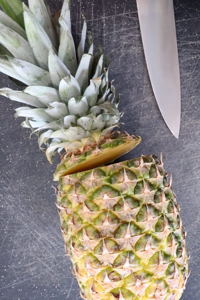 fresh pineapple with the crown cut off of the top on a cutting board