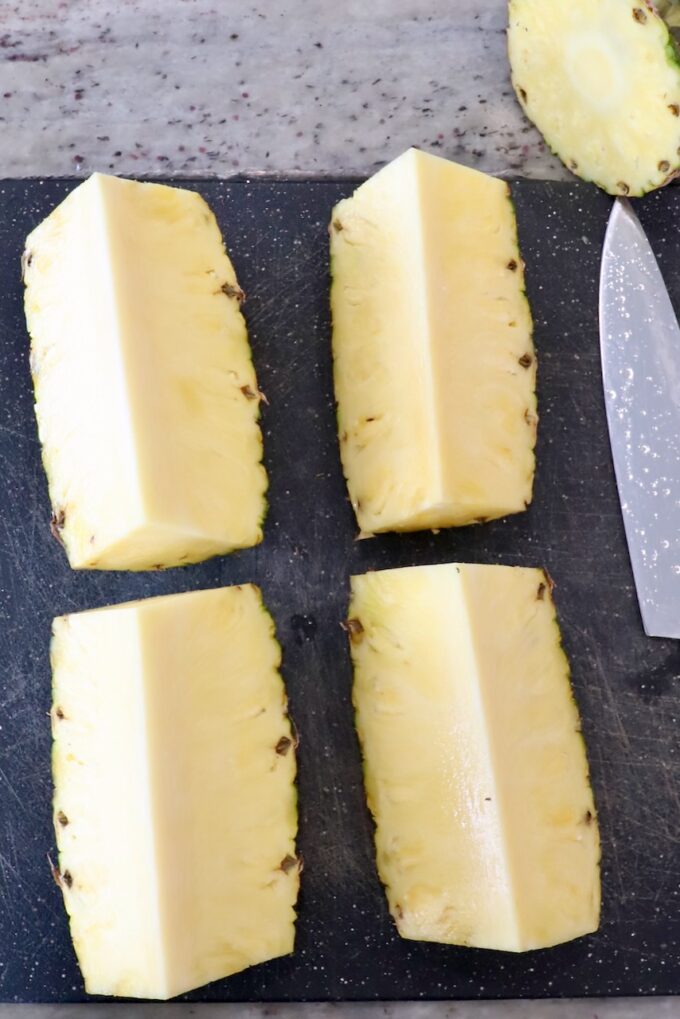 fresh pineapple sliced into four pieces on a cutting board