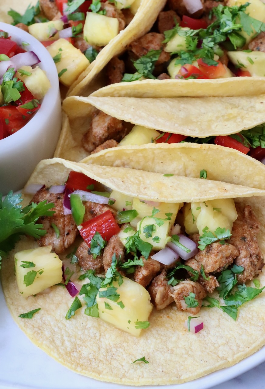 pork tacos topped with pineapple salsa on a plate