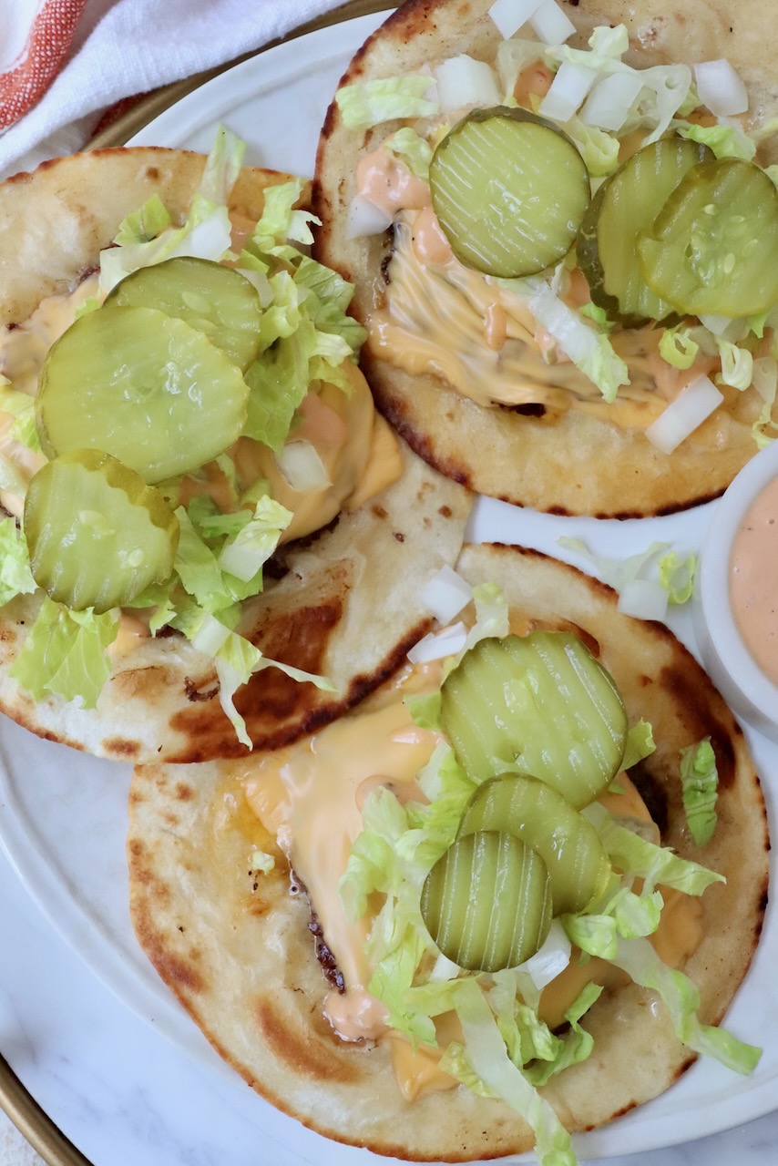 smash burger tacos on a plate topped with sliced pickles