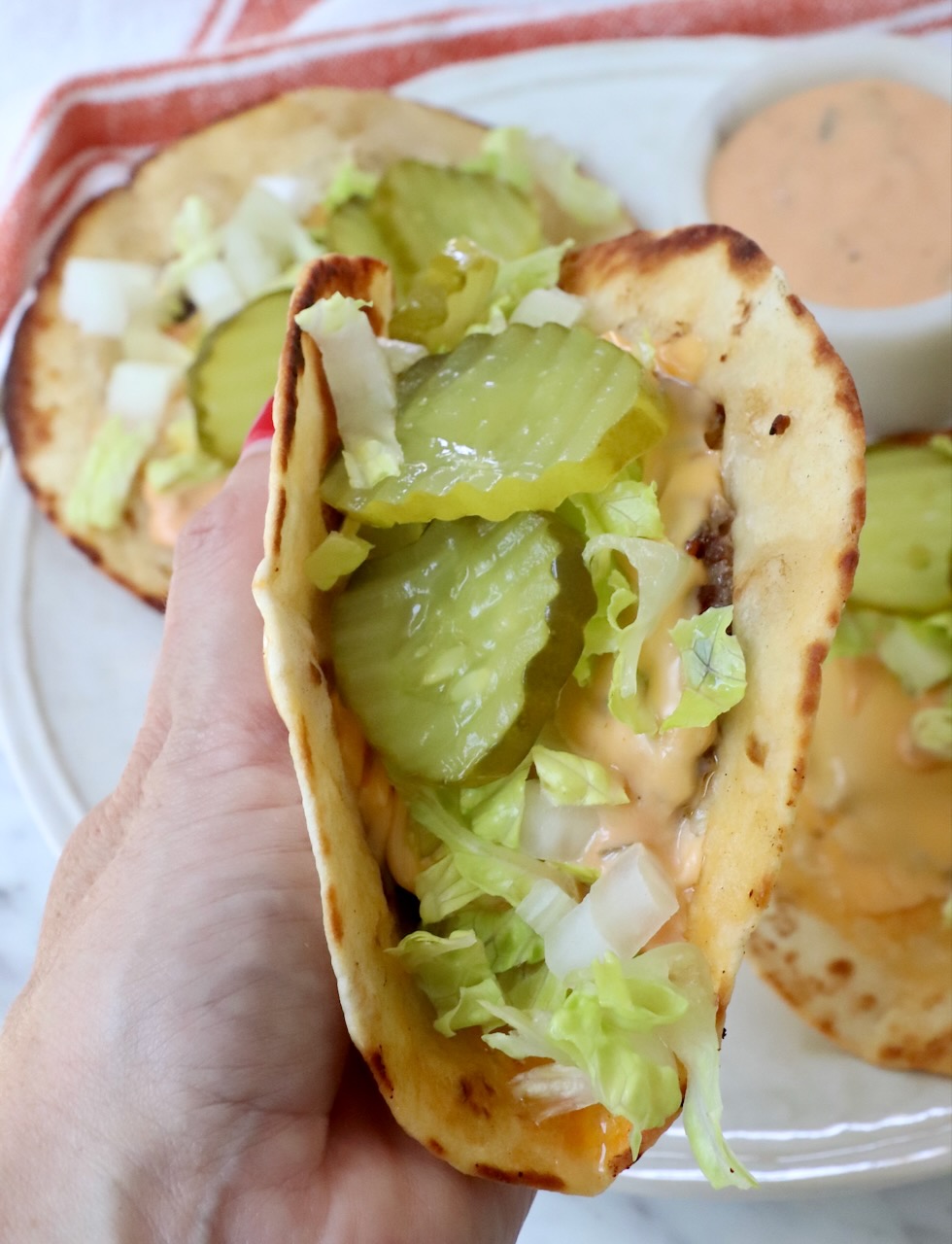 hand holding smash burger taco filled with pickles and lettuce over plate