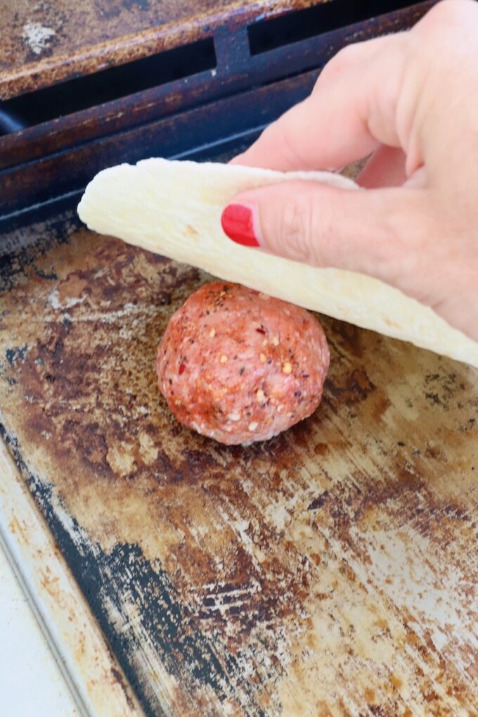 ball of beef on a griddle with a hand holding a tortilla above it