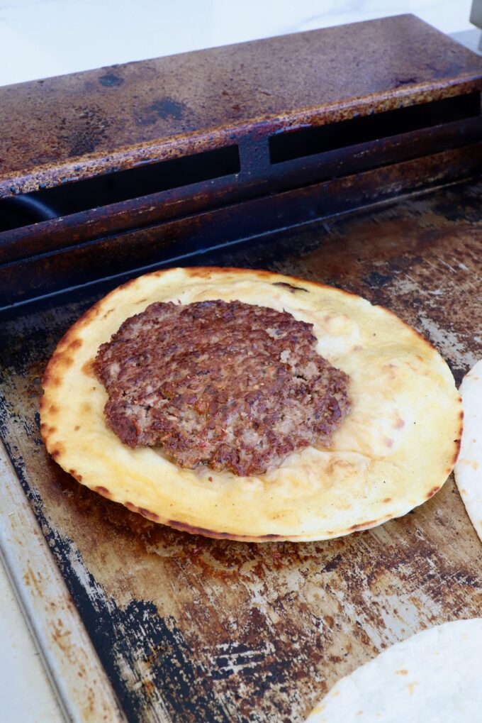 cooked burger patty on a tortilla on a griddle