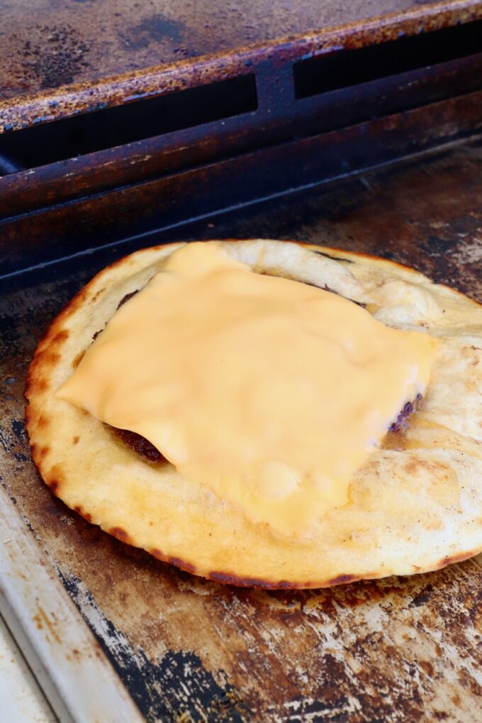 burger patty topped with a slice of cheese on a tortilla on a griddle