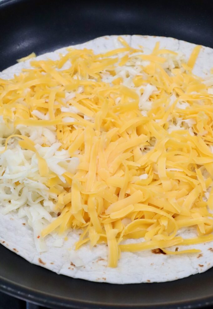 shredded cheese on tortilla in skillet