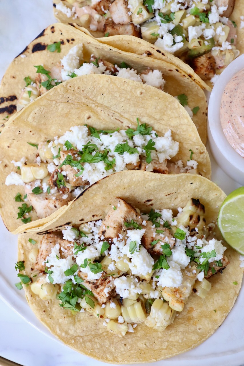 street corn and chicken tacos on plate with lime wedge