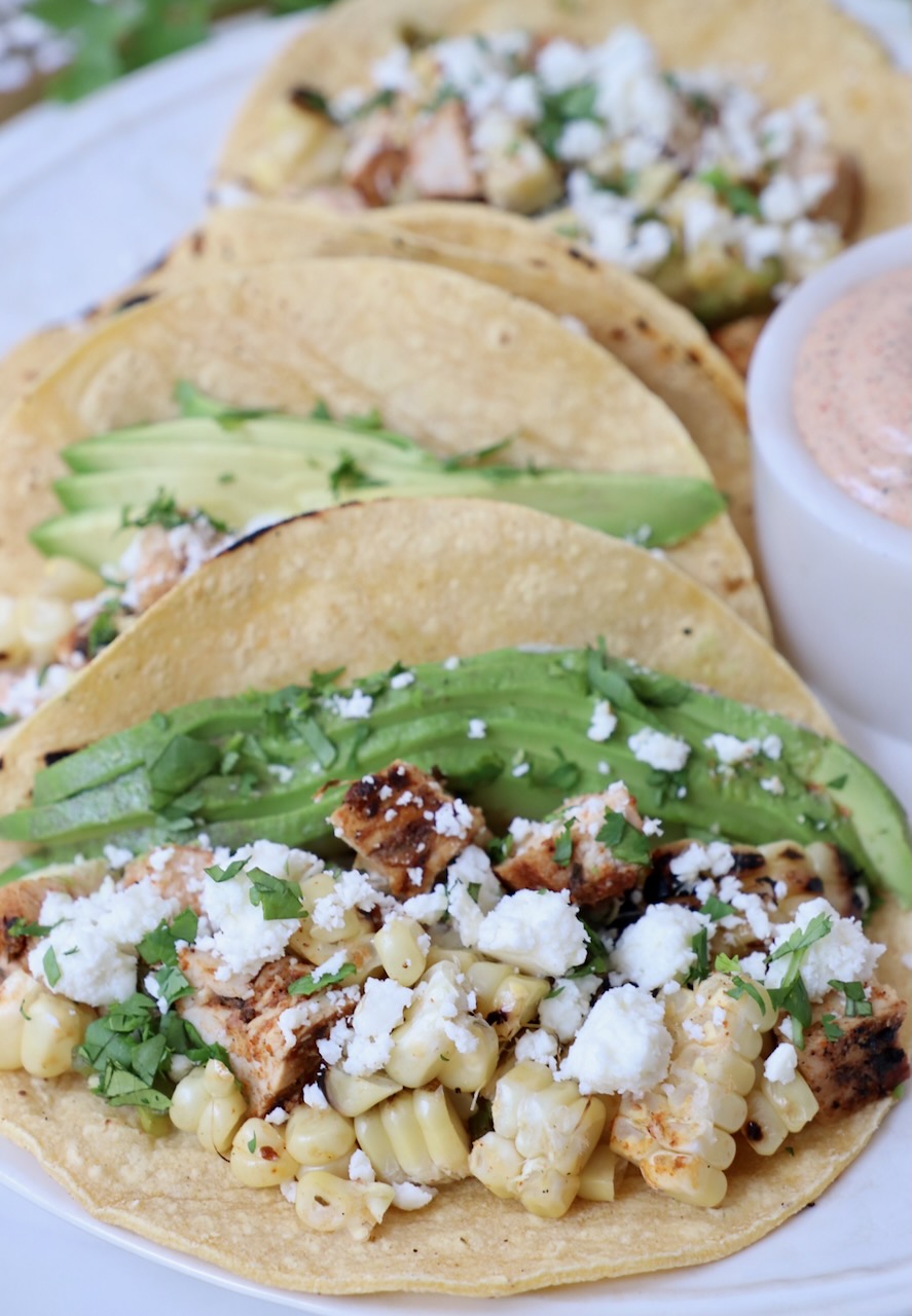 tacos on plate filled with diced chicken, corn and avocado